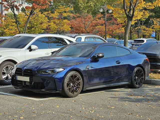 Side three-quarter view of a Tanzanite Blue 2022 BMW M4 Competition coupe
