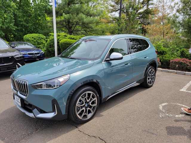 Front three-quarter view of a green 2024 BMW X1 xDrive28i in a parking lot